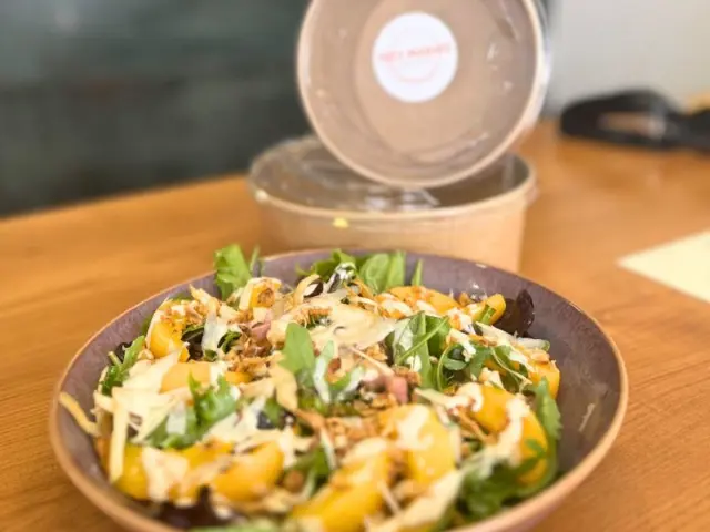 Uma salada numa taça de barro ao lado de uma embalagem para levar