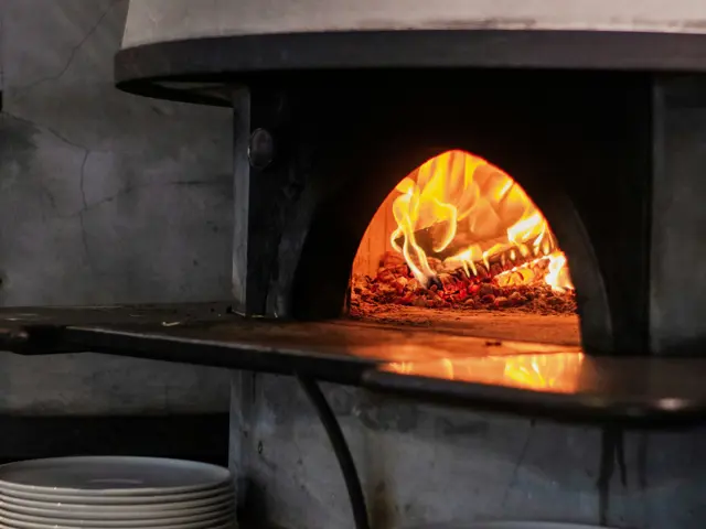 A boca do forno a lenha com a pizza lá dentro e as chamas ao lado