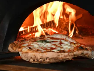 Uma pizza a cozer no forno a lenha, com o queijo ainda a borbulhar